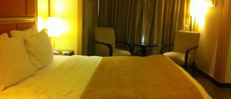 Una habitación de hotel con una cama grande, dos sillas, una mesita y una lámpara.