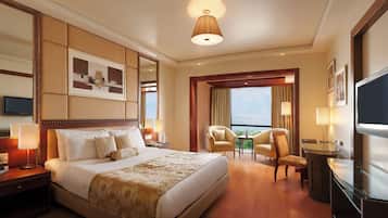 Habitación de hotel con una cama grande, televisión, escritorio con silla y vista al balcón.