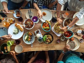 Um grupo de pessoas jantando em uma mesa de madeira, com diversos pratos e bebidas.