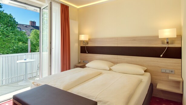 Een hotelkamer met een bed, nachtlampjes, een raam met gordijnen en een balkon.