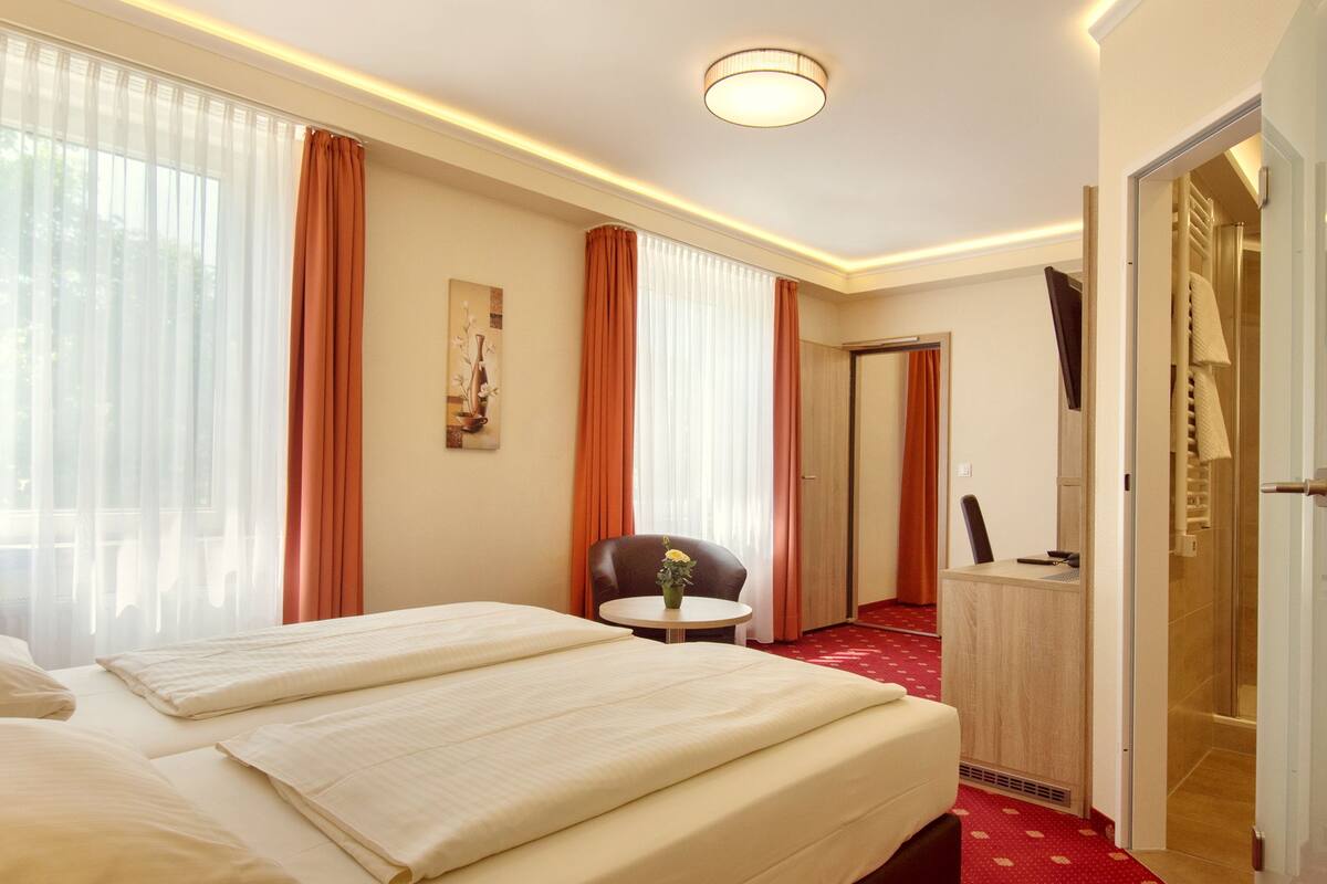 Habitación de hotel con dos camas, un escritorio, una silla y baño privado con ducha e inodoro.