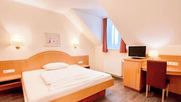 A hotel room with a bed, a desk, a television, and a window with curtains.