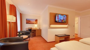 Een hotelkamer met een bed, een bureau, een stoel en een aan de muur bevestigde televisie.