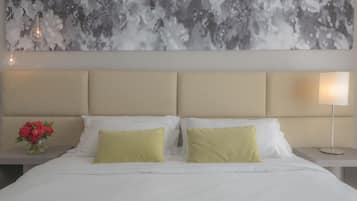 A hotel room with a large bed, two pillows, a vase with red flowers, a wall art piece, and a bedside lamp.