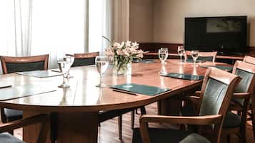 A conference room with a large oval table, wooden chairs, a vase of flowers, and a television on the wall.