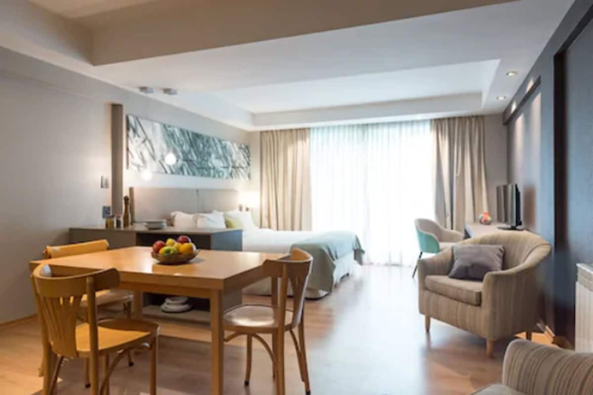Une chambre d’hôtel moderne comprenant un coin repas, un lit, une télévision et une grande fenêtre avec des rideaux.