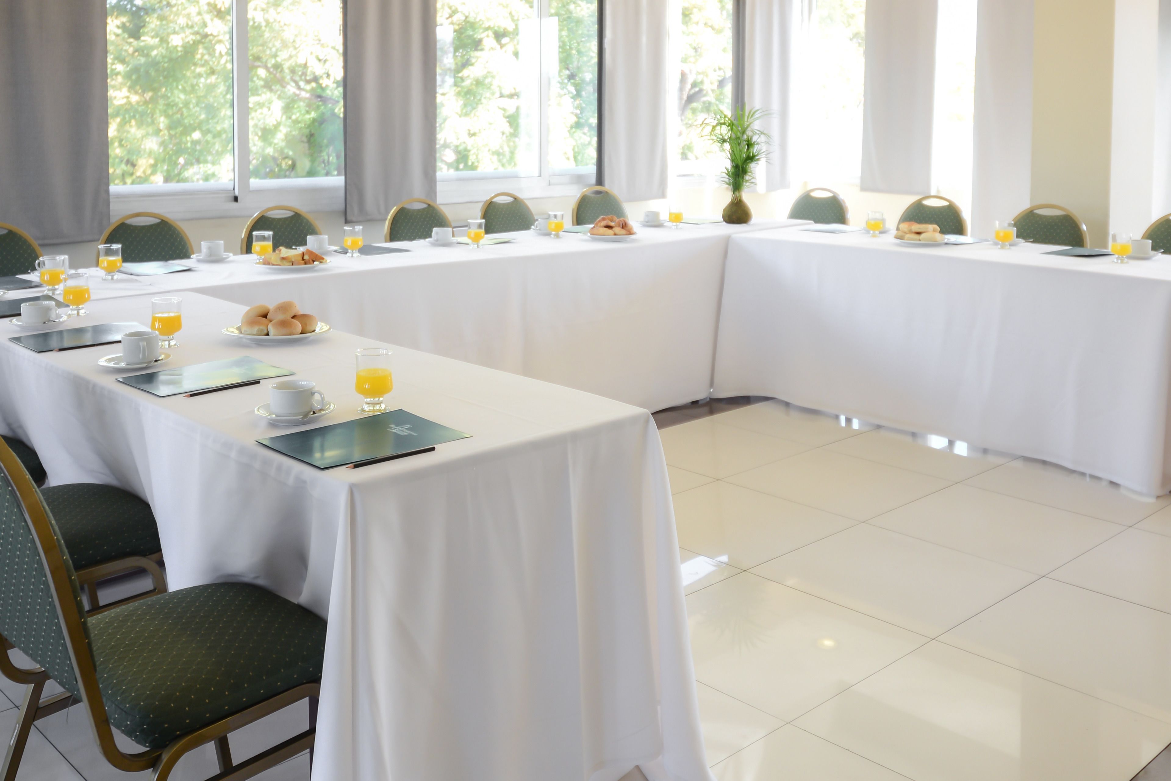 A conference room with a long table set for breakfast, including plates of pastries and glasses of orange juice.