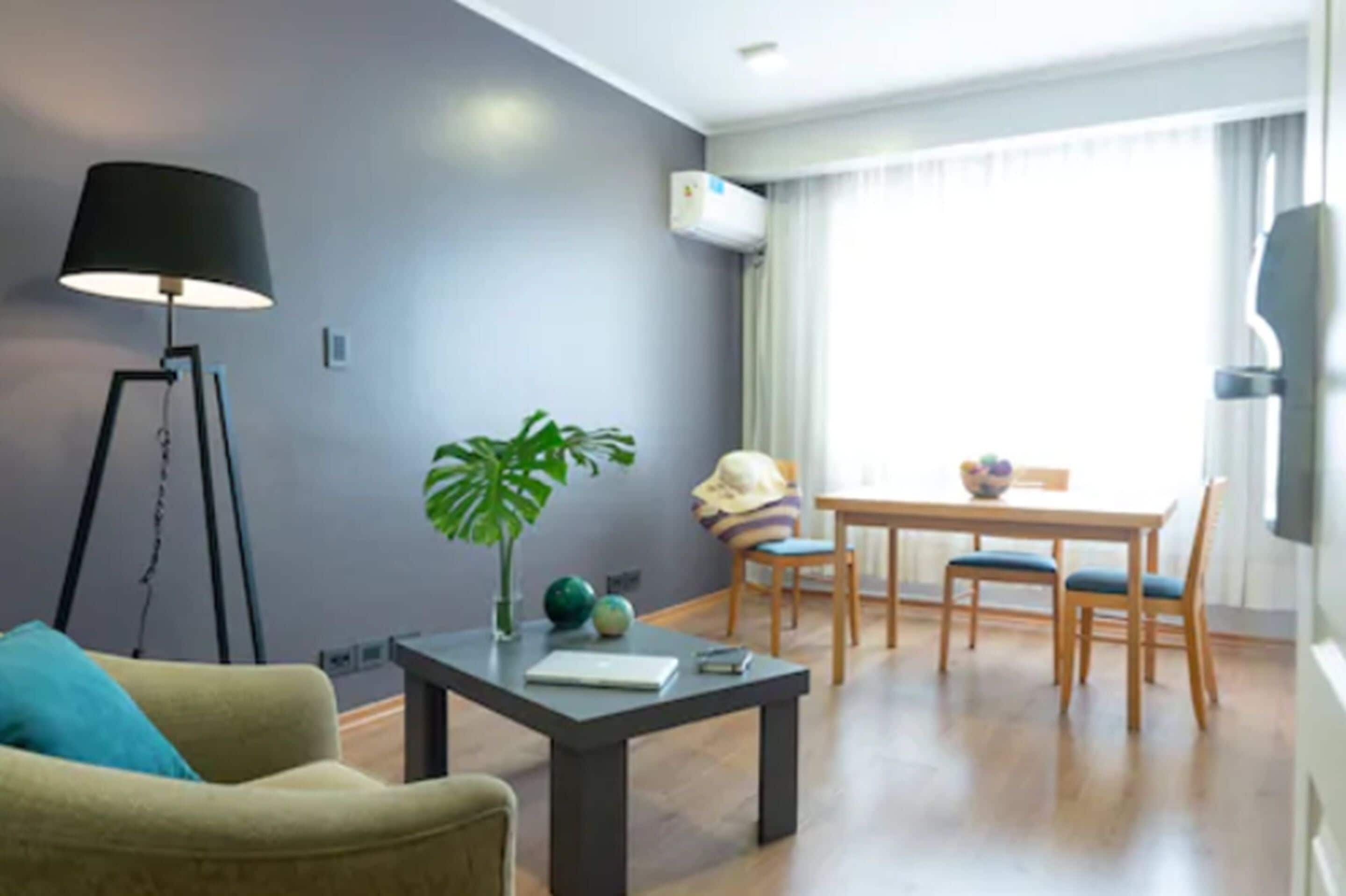 A modern living room with a sofa, a coffee table, a floor lamp, a dining table with chairs, and a potted plant.