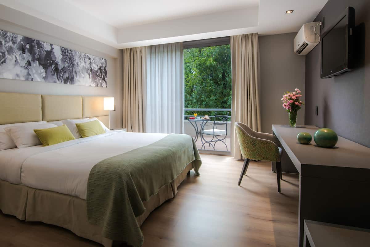 Une chambre d’hôtel équipée d’un lit, d’un bureau, d’une chaise, d’une télévision et d’un balcon donnant sur un paysage verdoyant.