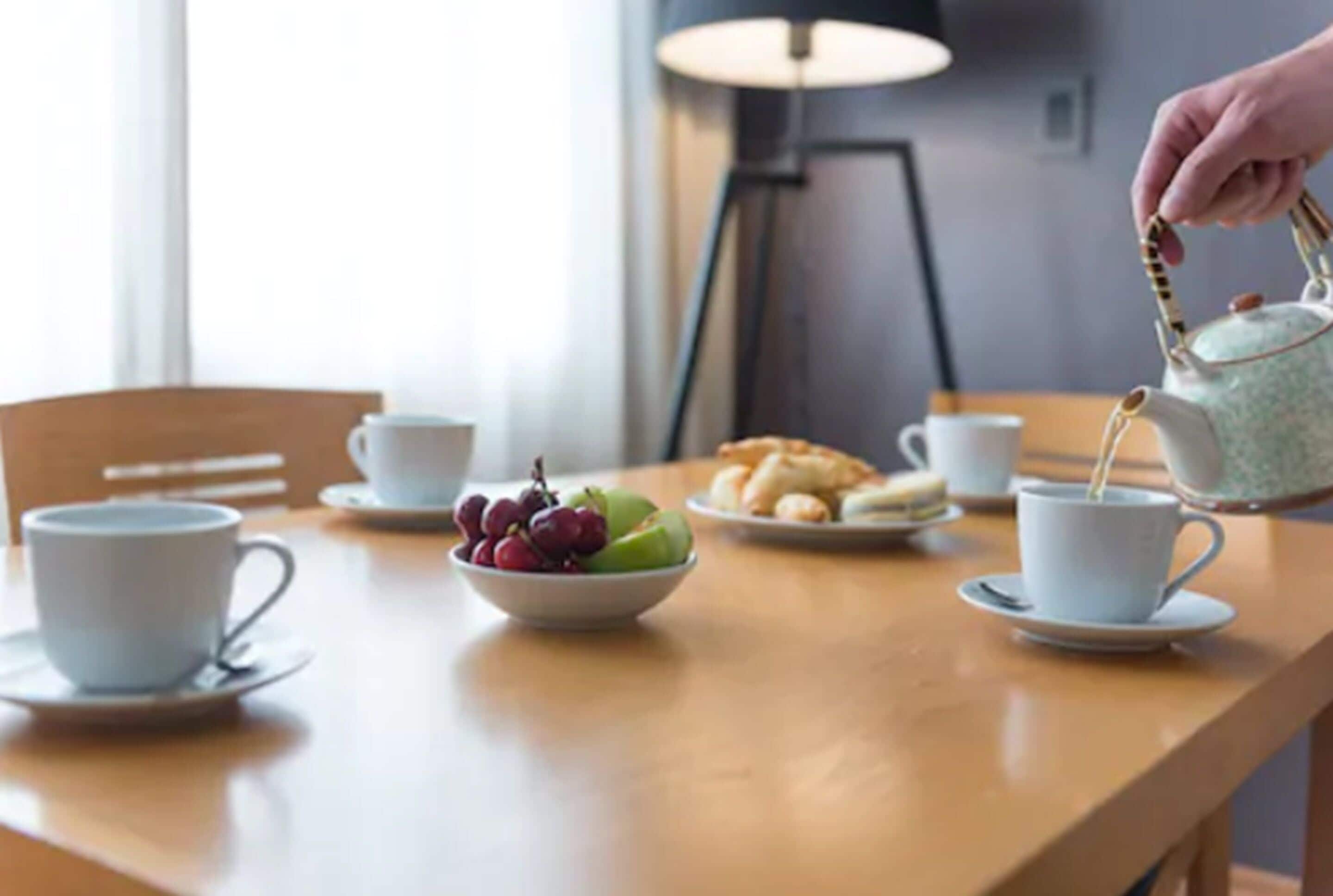 A wooden table with a white cup, a bowl of fruit, and a teapot.