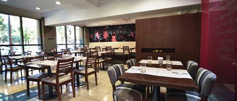 Un comedor amplio con varias mesas y sillas, ventanas grandes y un mural decorativo en la pared.