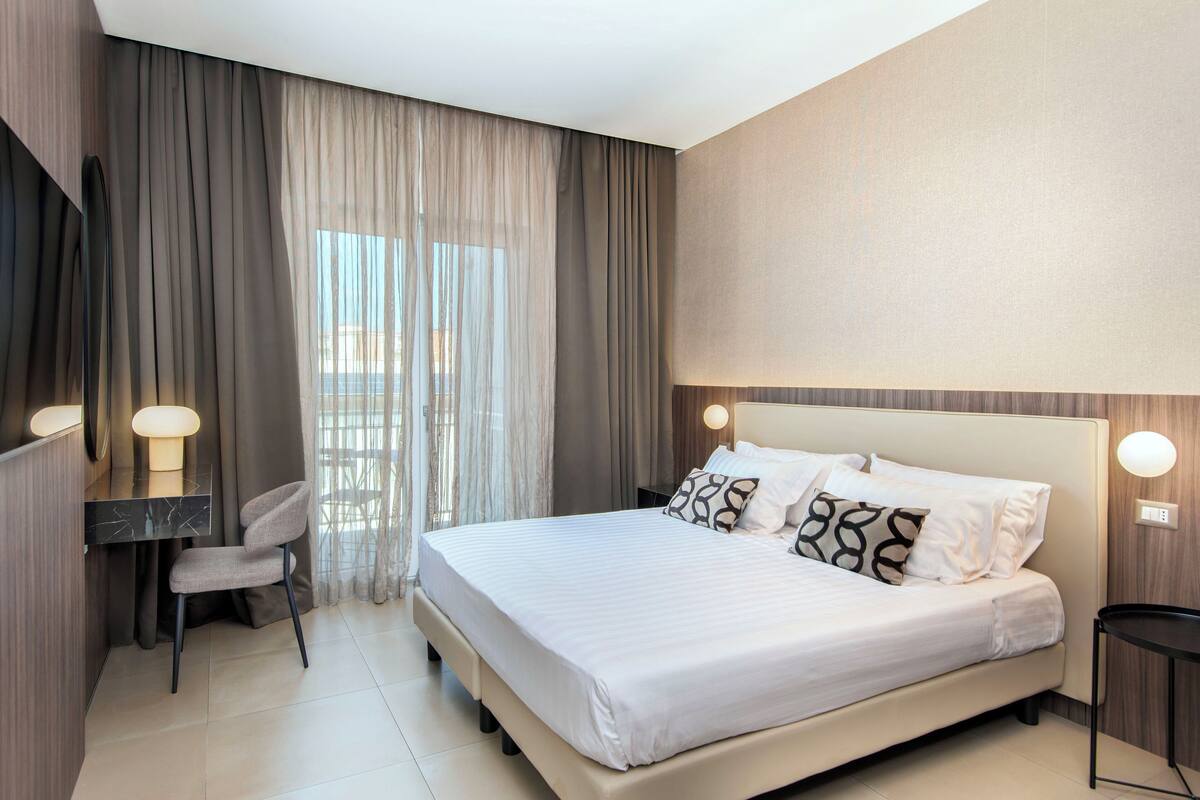 A modern hotel room with a large bed, a desk, and a chair.