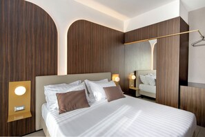 Una habitación de hotel moderna con una cama grande, una mesita de noche con lámpara y un espejo en la pared.