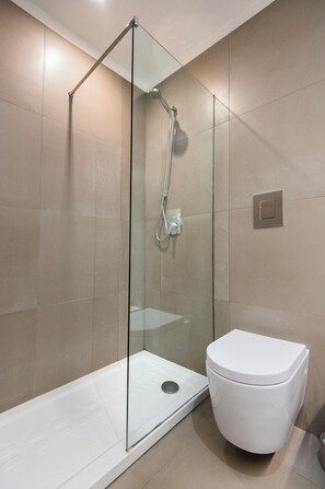 Un baño moderno con ducha de vidrio, inodoro blanco y paredes con azulejos color beige.