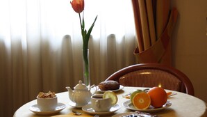A table set with breakfast items including a teapot, cups, a bowl of cereal, a plate with a pastry, and a plate with an orange and a slice of lemon. - Hotel Europa (Arzano)