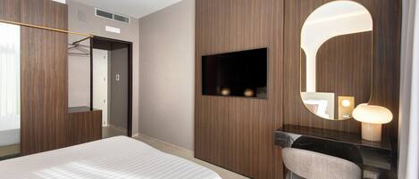 A modern hotel room with a large bed, a desk with a chair, a TV, and a mirror.