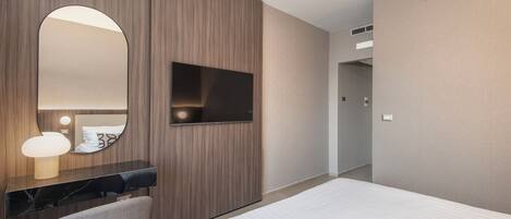 Una habitación de hotel con cama, escritorio, silla, televisor y espejo.