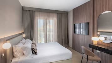 Habitación de hotel con cama, escritorio, silla, televisor y un amplio ventanal con cortinas.