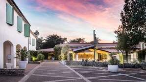 A courtyard with a building featuring a tiled roof and a bar area. There are bicycles parked outside and potted plants around the area. - Hotel Les Grenettes (Sainte-Marie-de-Re)
