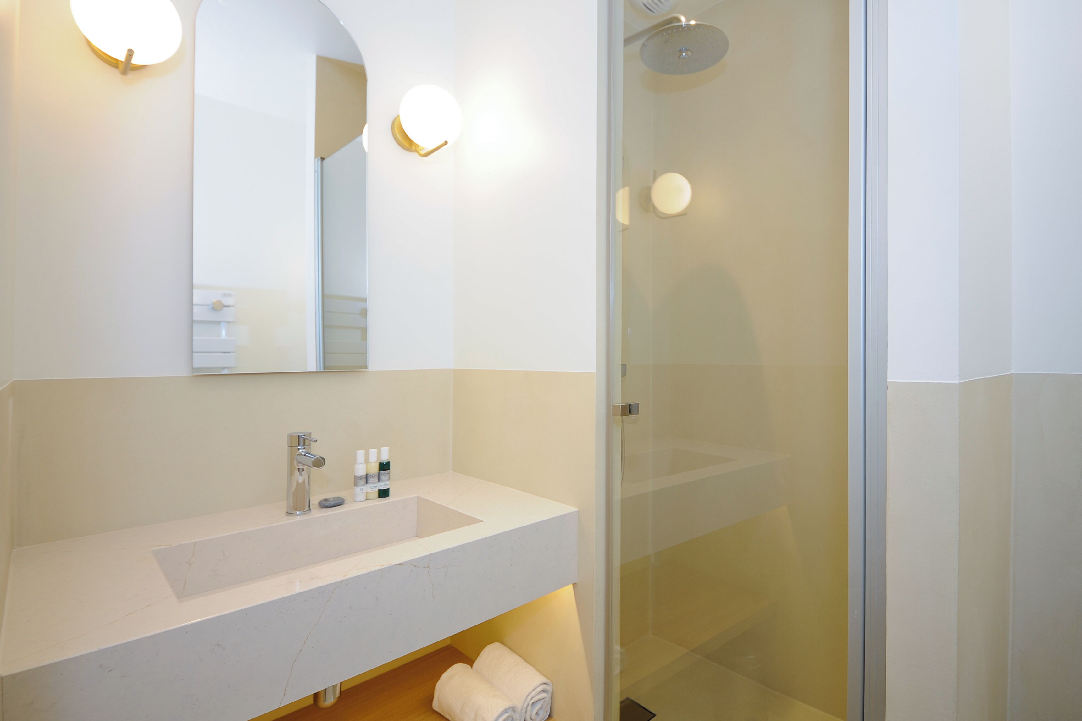 A modern bathroom with a white sink, mirror, and glass shower enclosure.