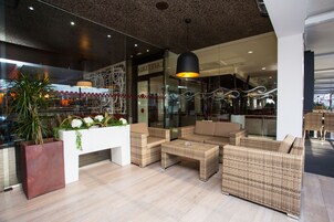 Un lobby moderno con mobiliario de mimbre, un mostrador de recepción blanco y un amplio ventanal.