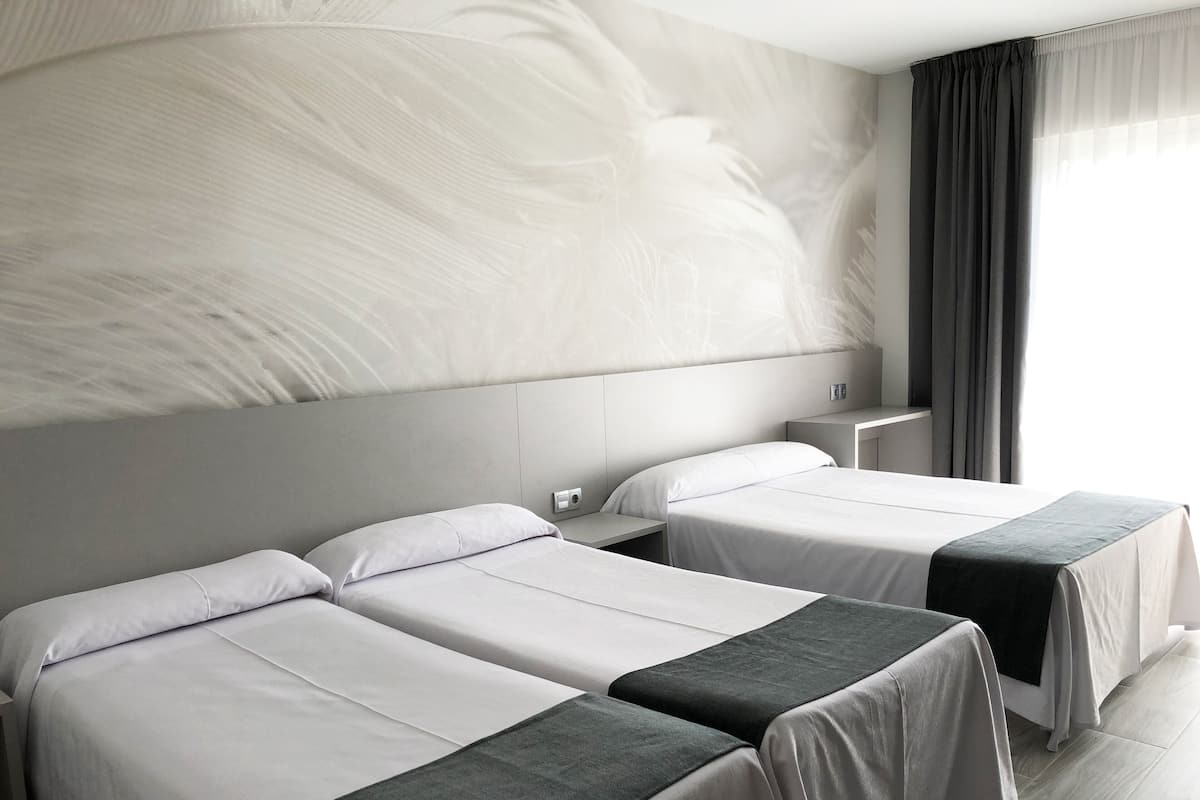 Ein Hotelzimmer mit zwei Betten, einem großen abstrakten Wandbild, einem Nachttisch mit Lampe und einem Fenster mit Vorhängen.