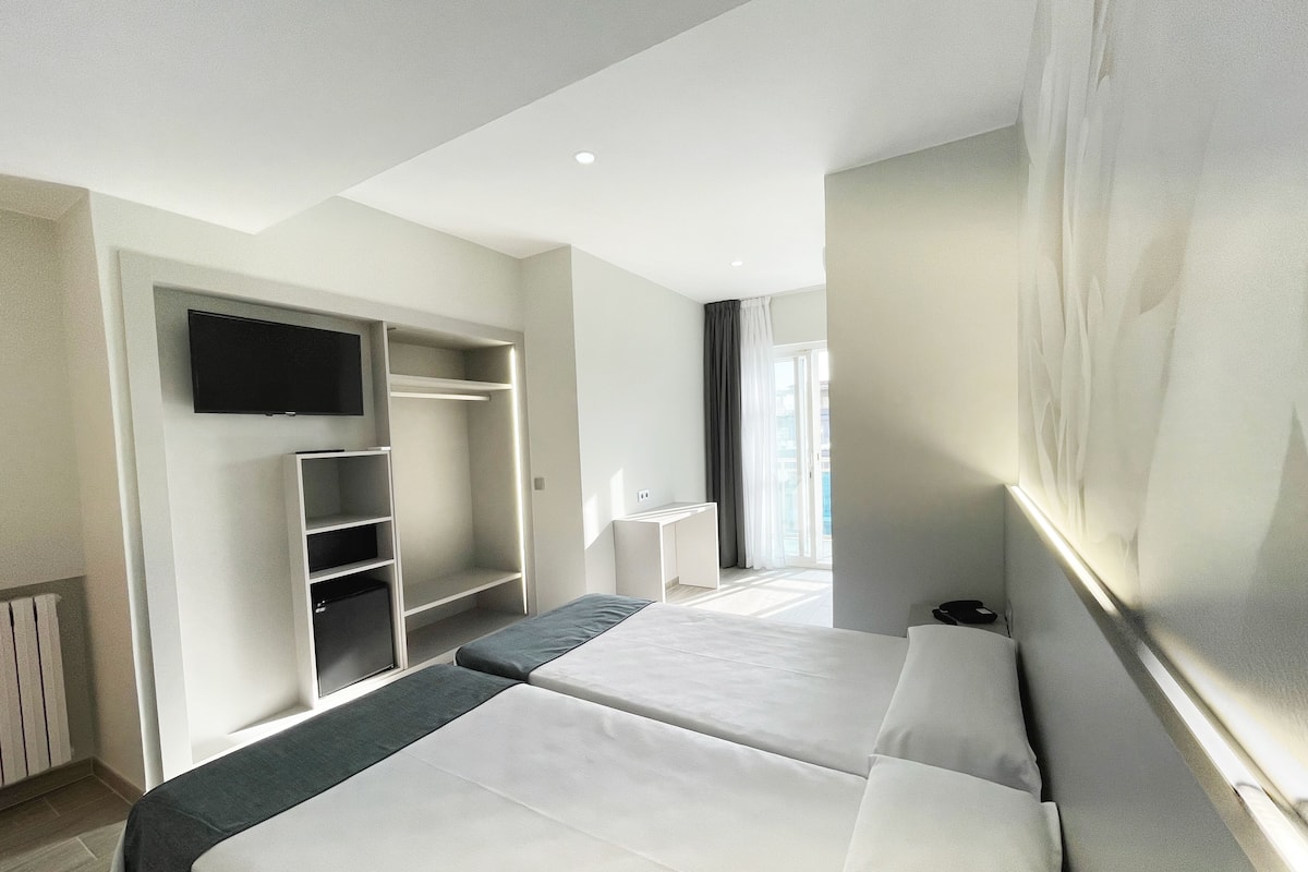 Ein Hotelzimmer mit zwei Betten, einem Wand-Fernseher, einem Schreibtisch und einem Kleiderschrank.