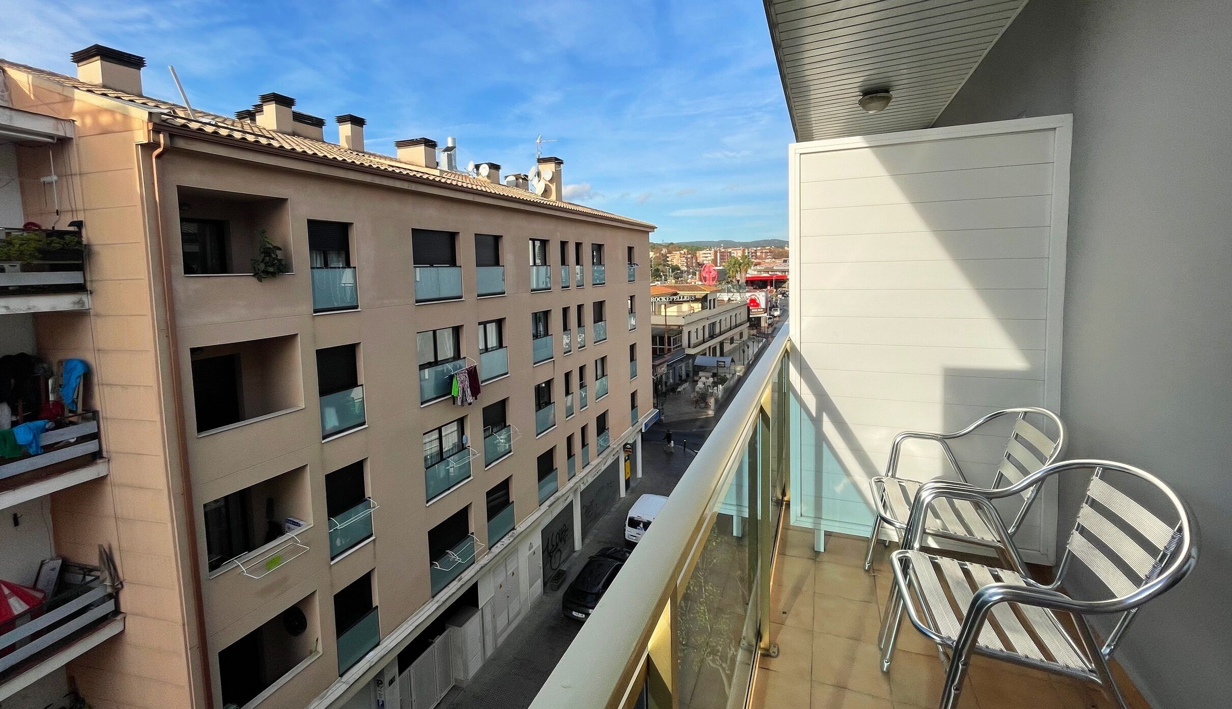 Un immeuble à plusieurs étages, doté de balcons, offrant une vue sur la rue et s’ouvrant sur un ciel dégagé.