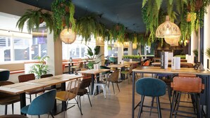 Interior de restaurante con mesas y sillas de madera, plantas colgantes e iluminación colgante.