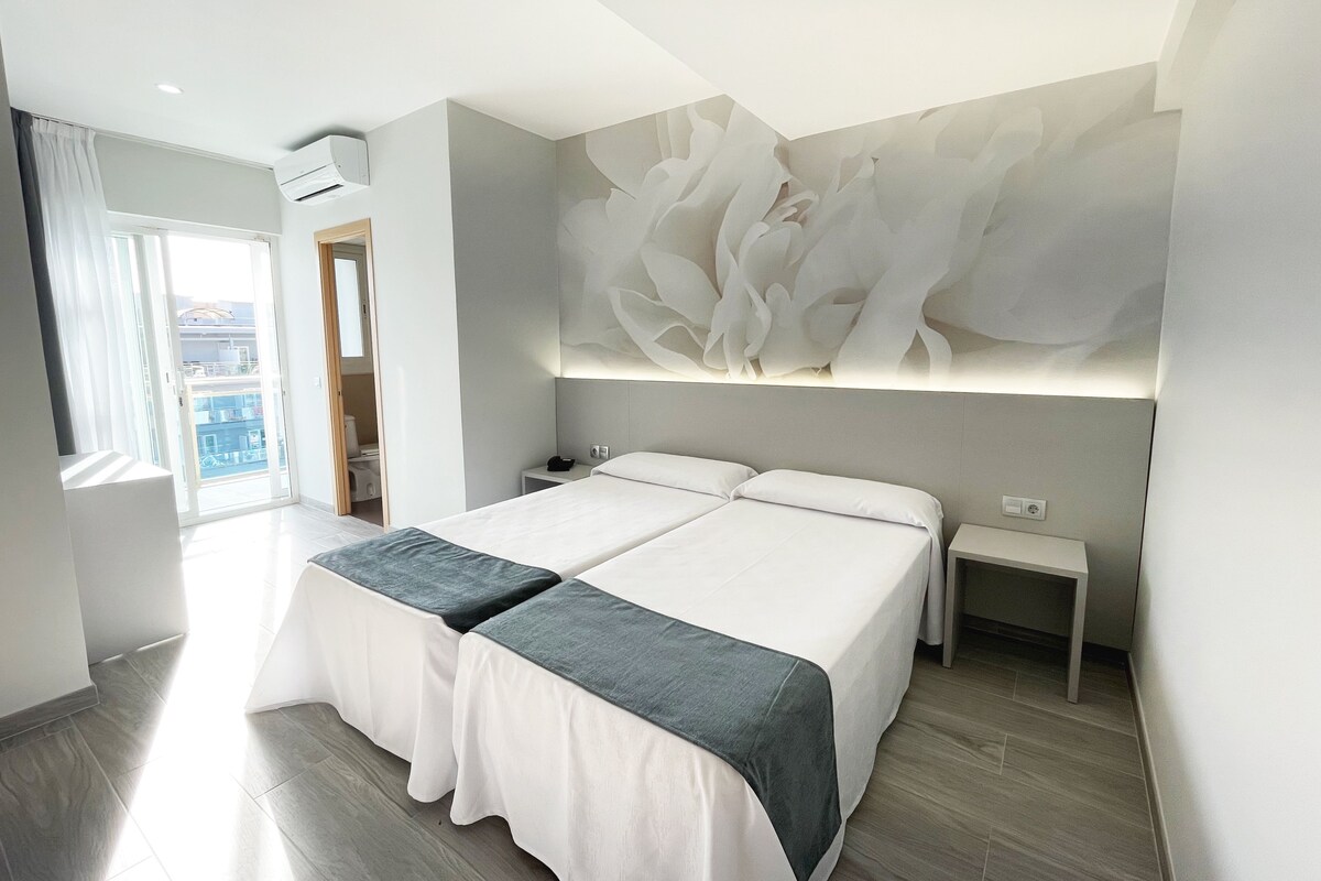 Une chambre moderne avec un grand lit, deux tables de chevet et un climatiseur fixé au mur.
