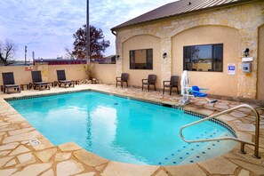 A swimming pool with a stone border, lounge chairs, and a building with a stone facade. - Days Inn & Suites by Wyndham Llano (Llano)