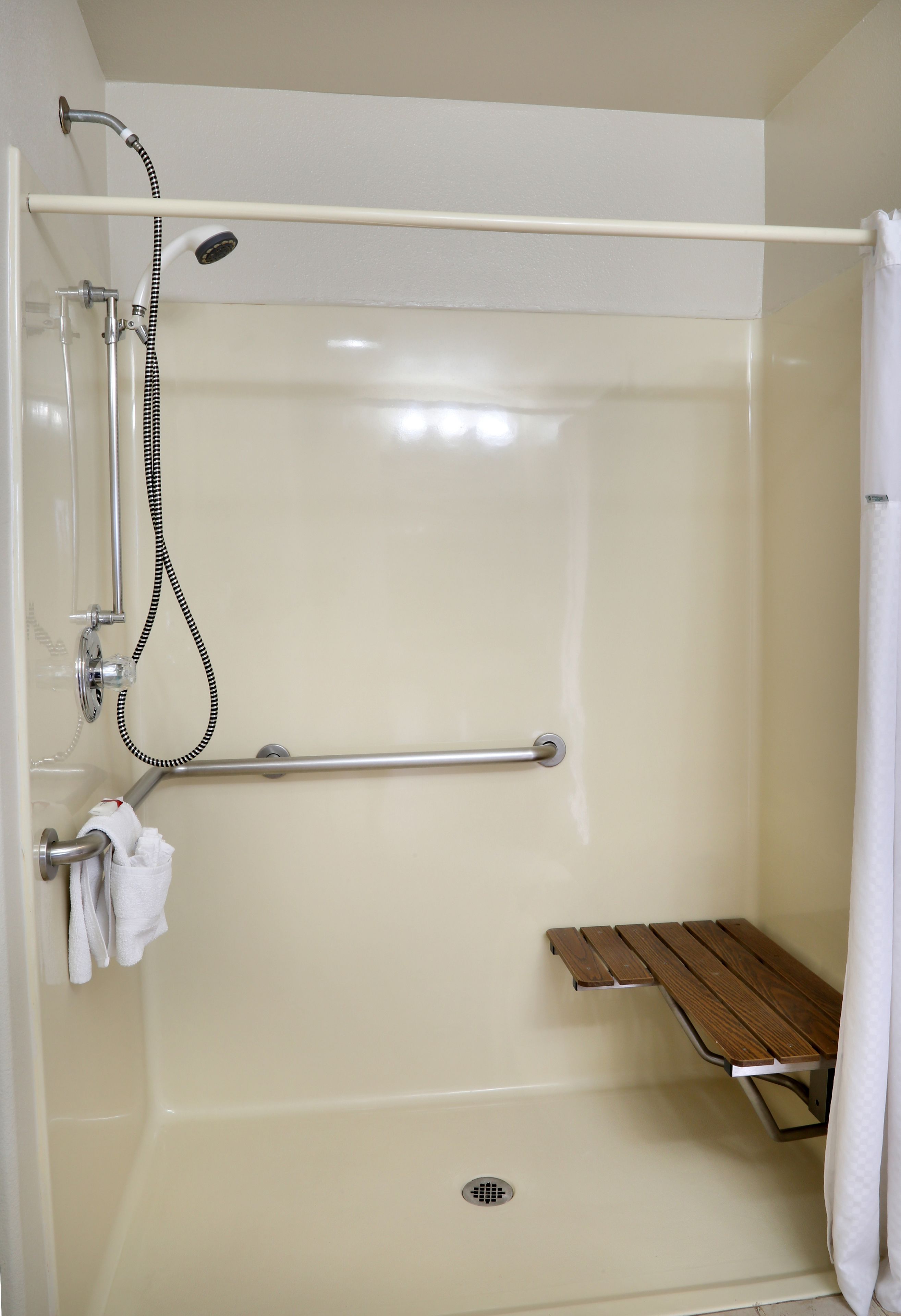 A walk-in shower with a grab bar, a bench, and a towel rack.