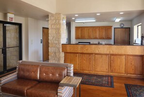 A modern kitchen with wooden cabinets and a stone pillar, a brown leather sofa, and a small table. - Days Inn & Suites by Wyndham Llano (Llano)