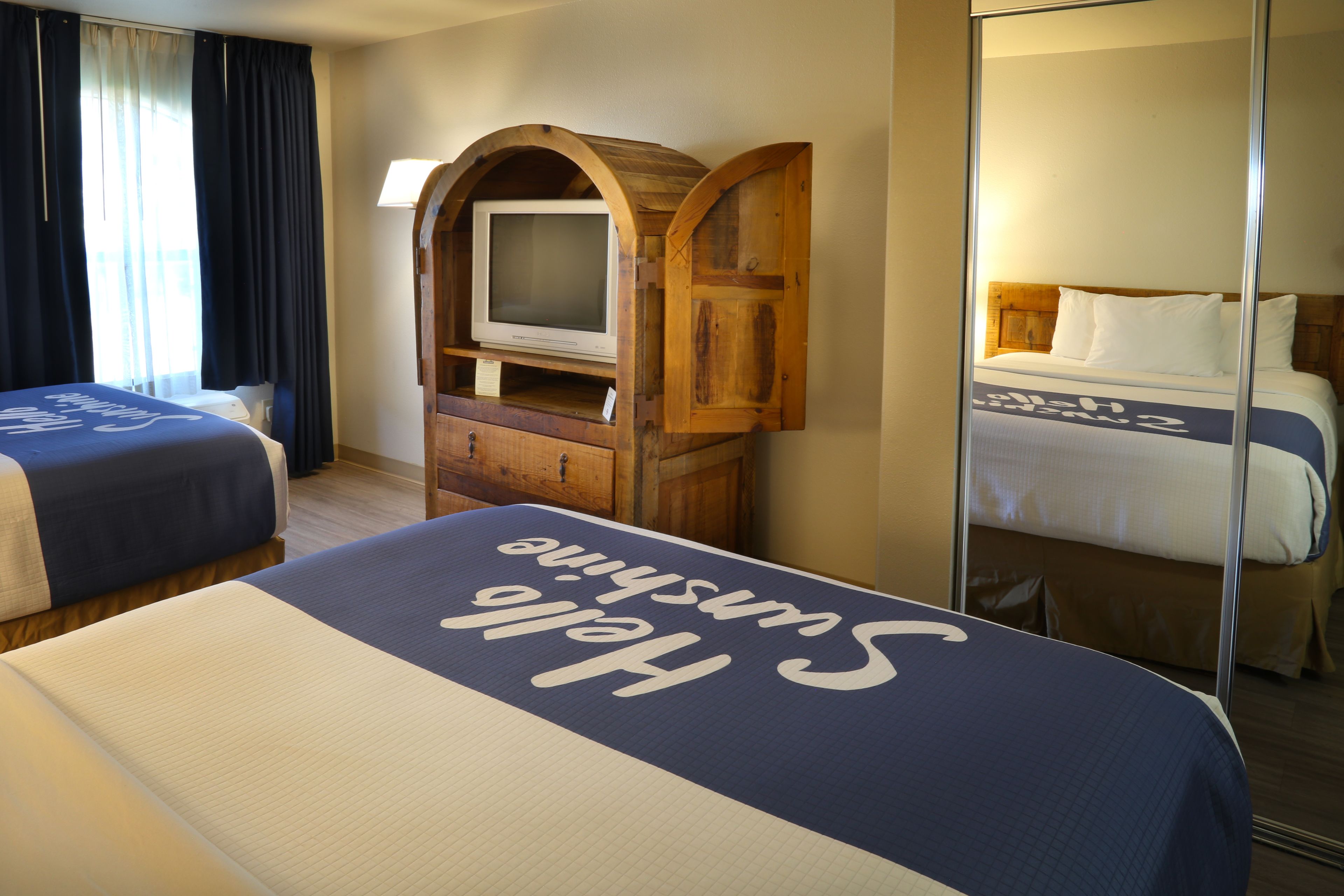 Habitación de hotel con dos camas, un televisor en un mueble de madera y un espejo que refleja la cama.