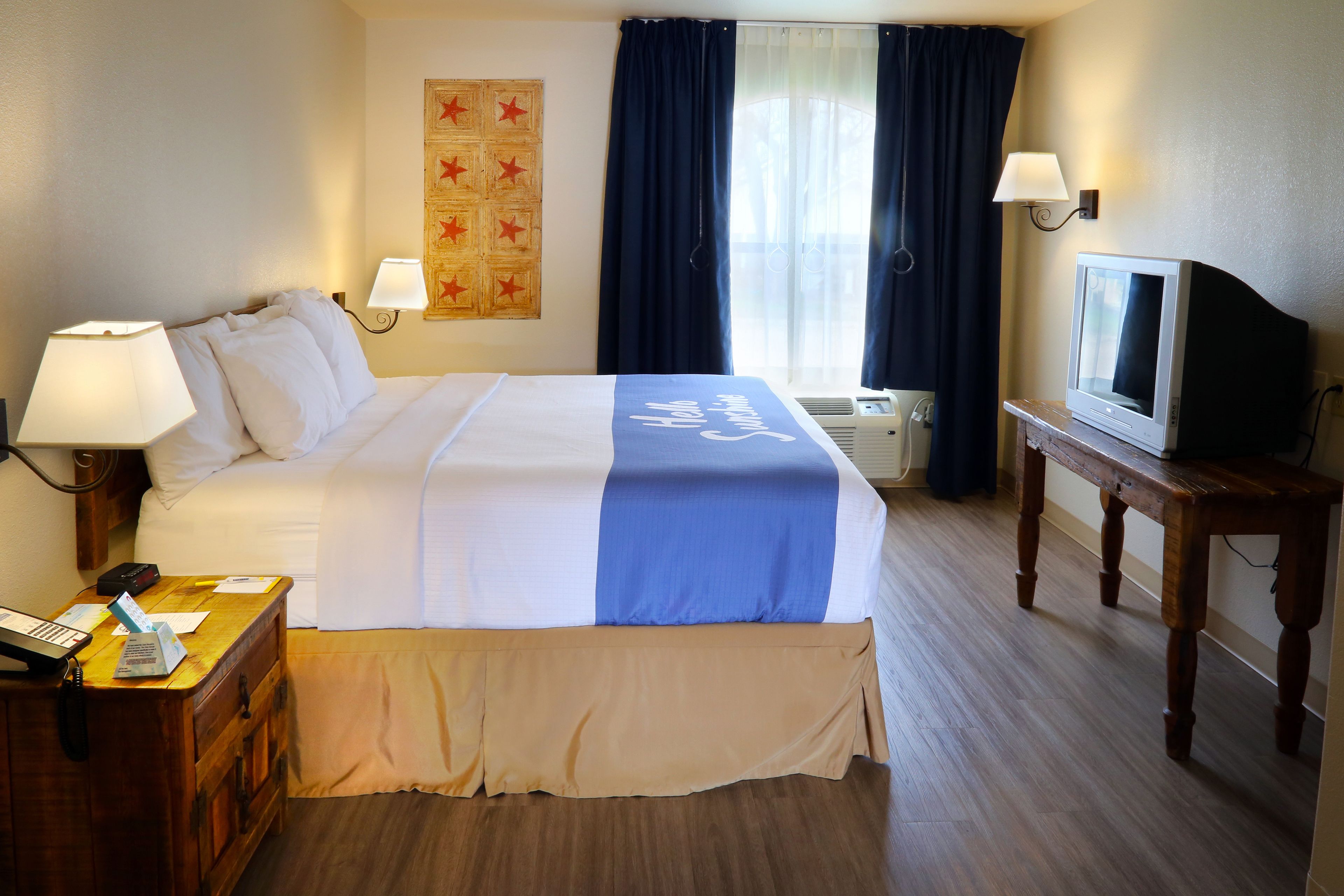 Habitación de hotel con cama, escritorio con lámpara, televisor y calefacción en la pared.