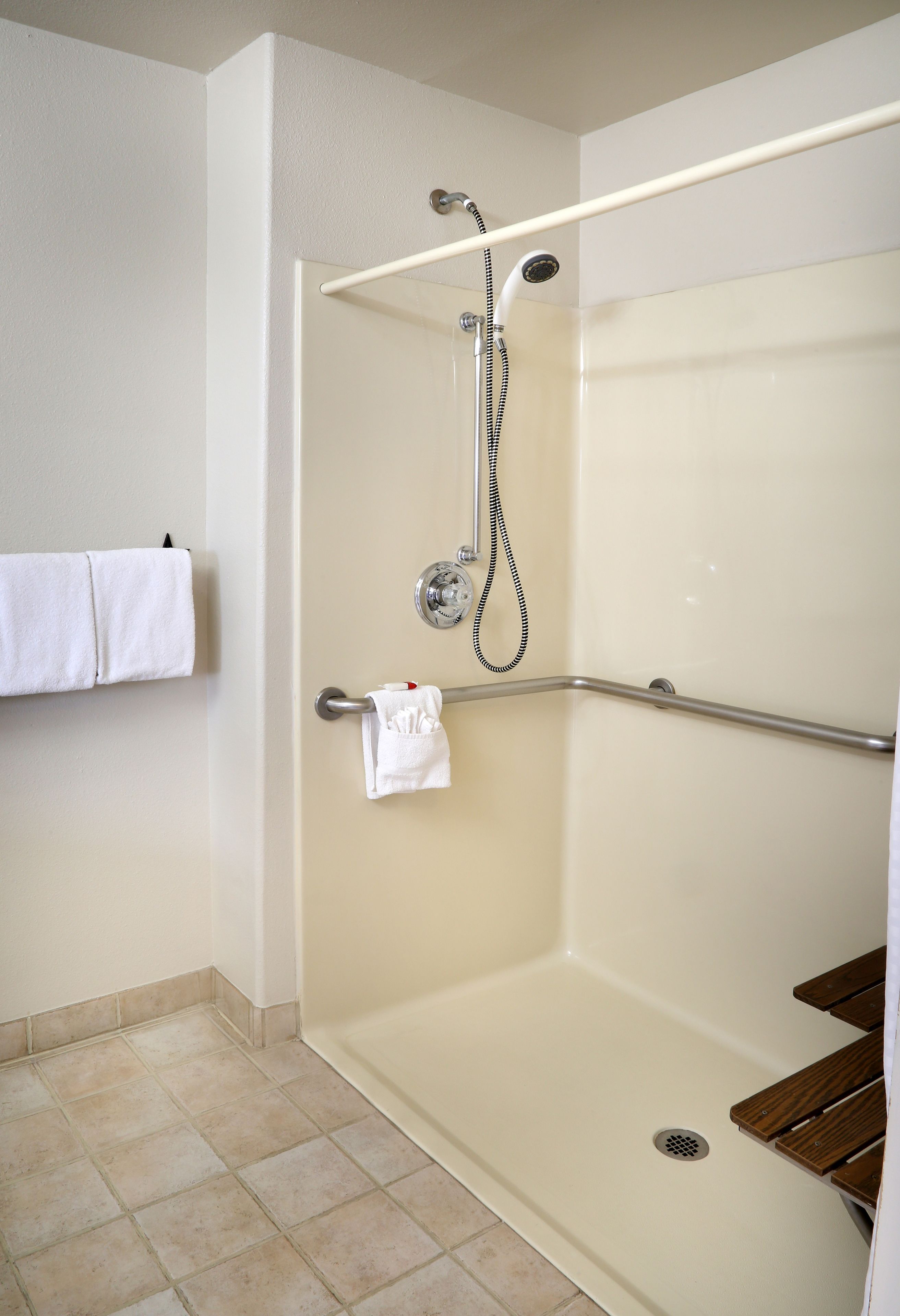 Une douche à l’italienne équipée d’une barre d’appui, d’un porte-serviettes et d’un banc en bois.