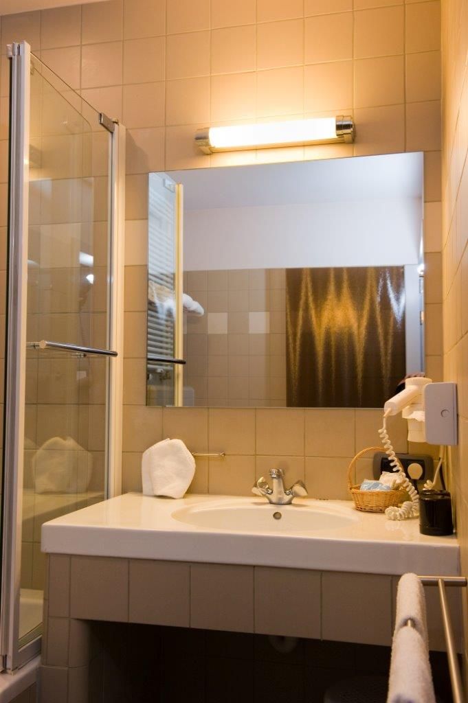 Een badkamer met een douchecabine van glas, een witte wastafel, een spiegel en een handdoekhouder.
