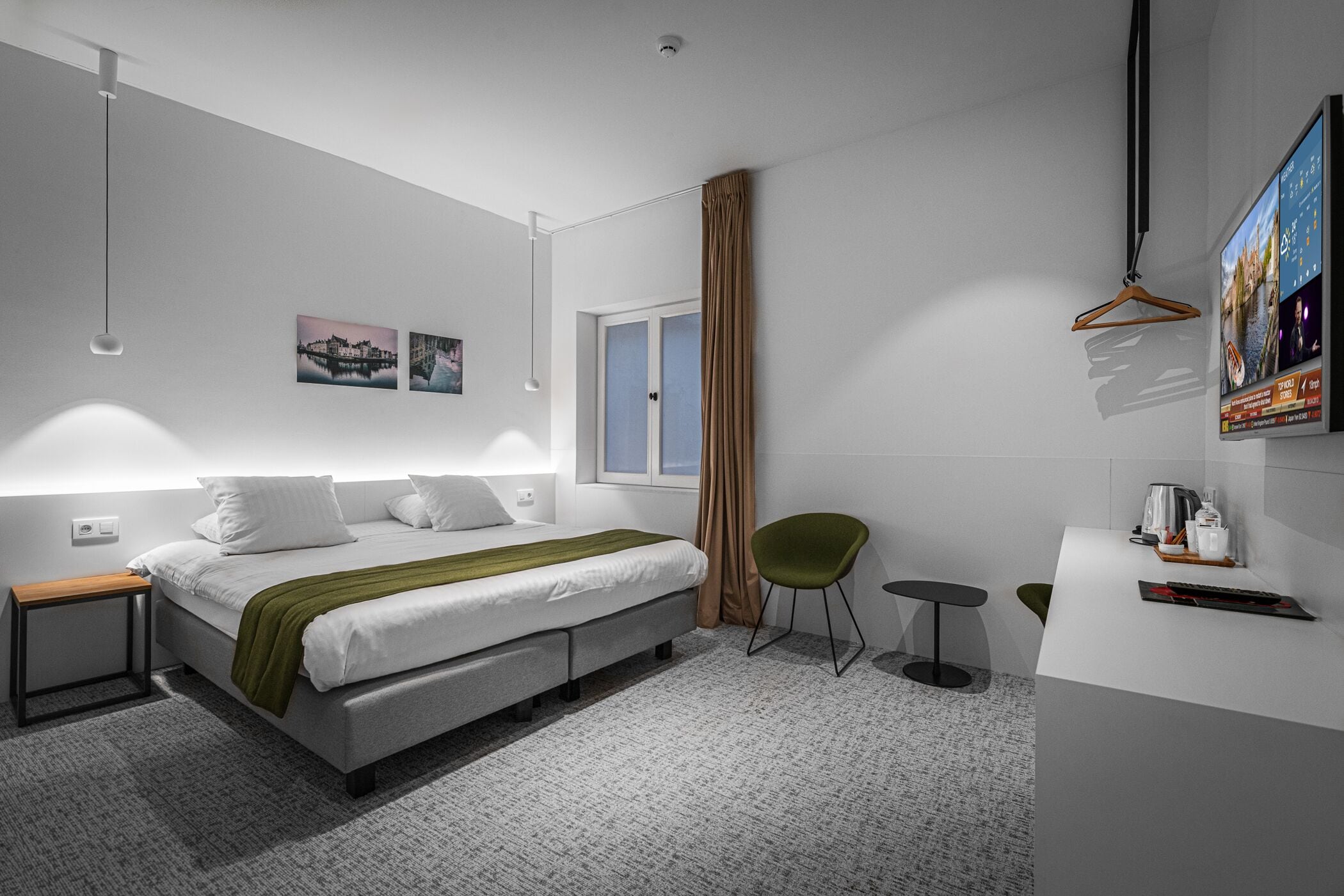 Una habitación de hotel moderna con cama, mesitas de noche, escritorio, silla, perchero y un ventanal grande.