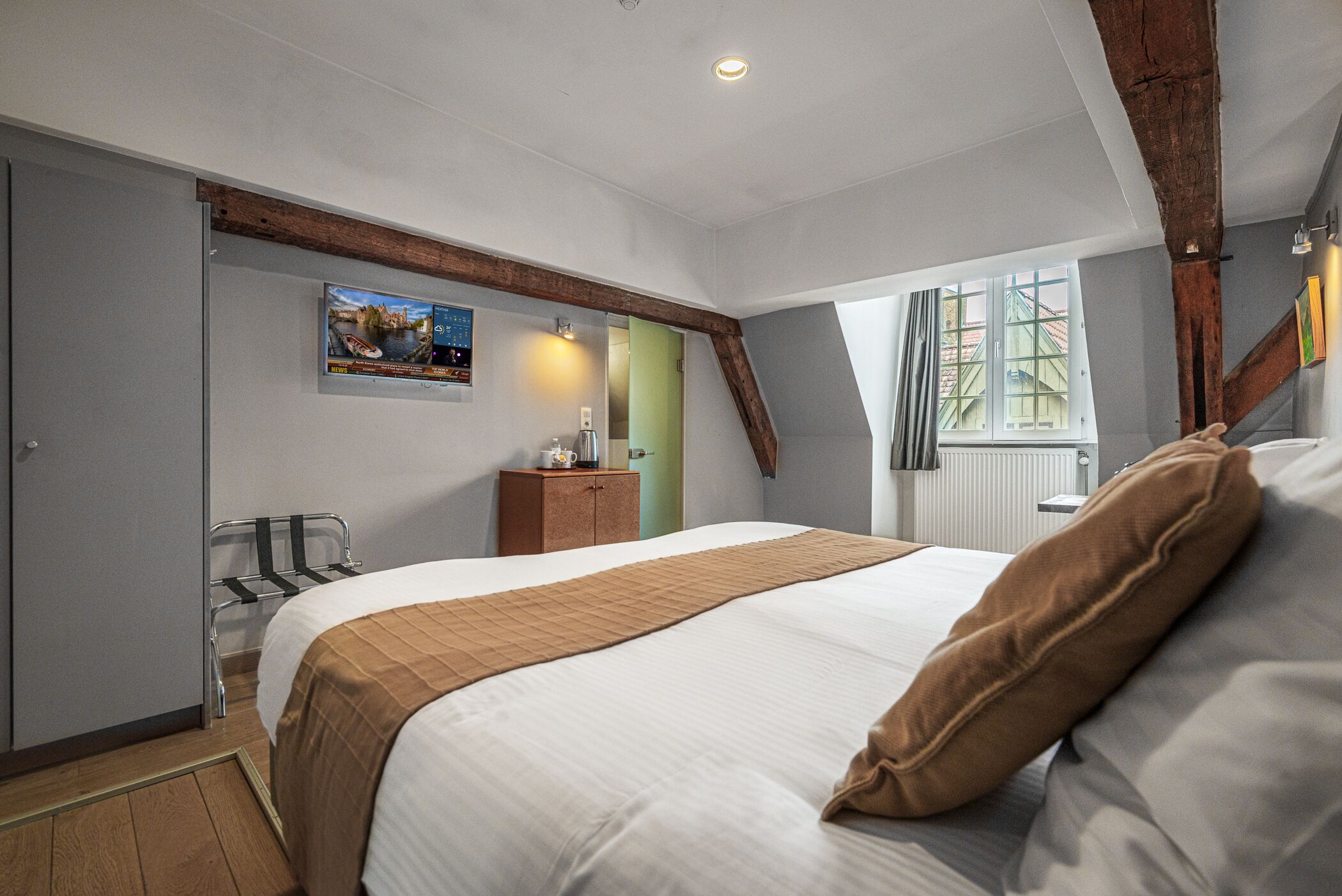 Una habitación de hotel con una cama grande, cabecera de madera, un escritorio pequeño y una ventana con cortinas.