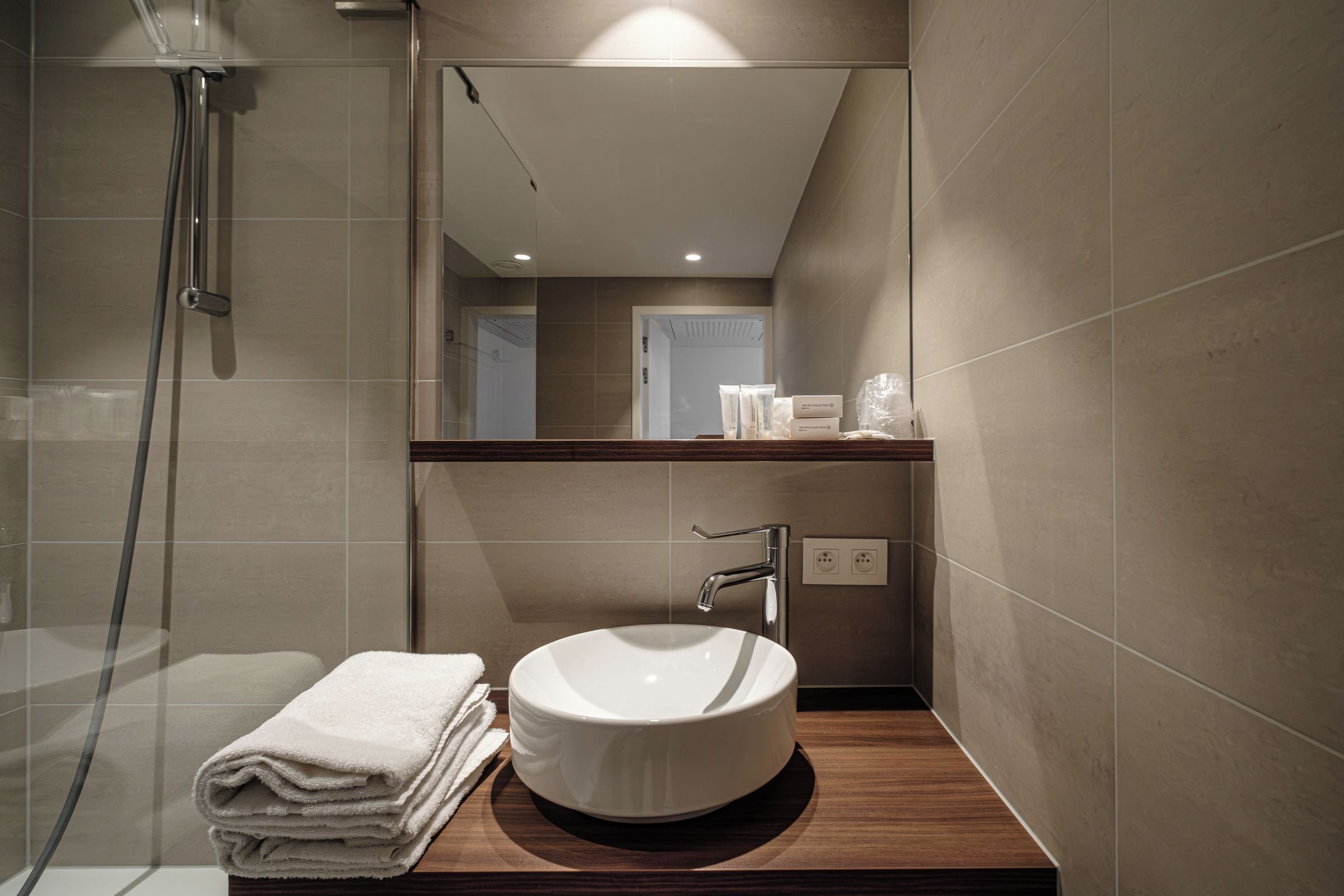 A modern bathroom with a glass shower enclosure, a round sink, and a wooden countertop.