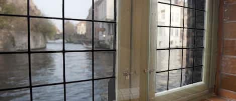 A window with a grid pattern, overlooking a canal with buildings and a bridge.