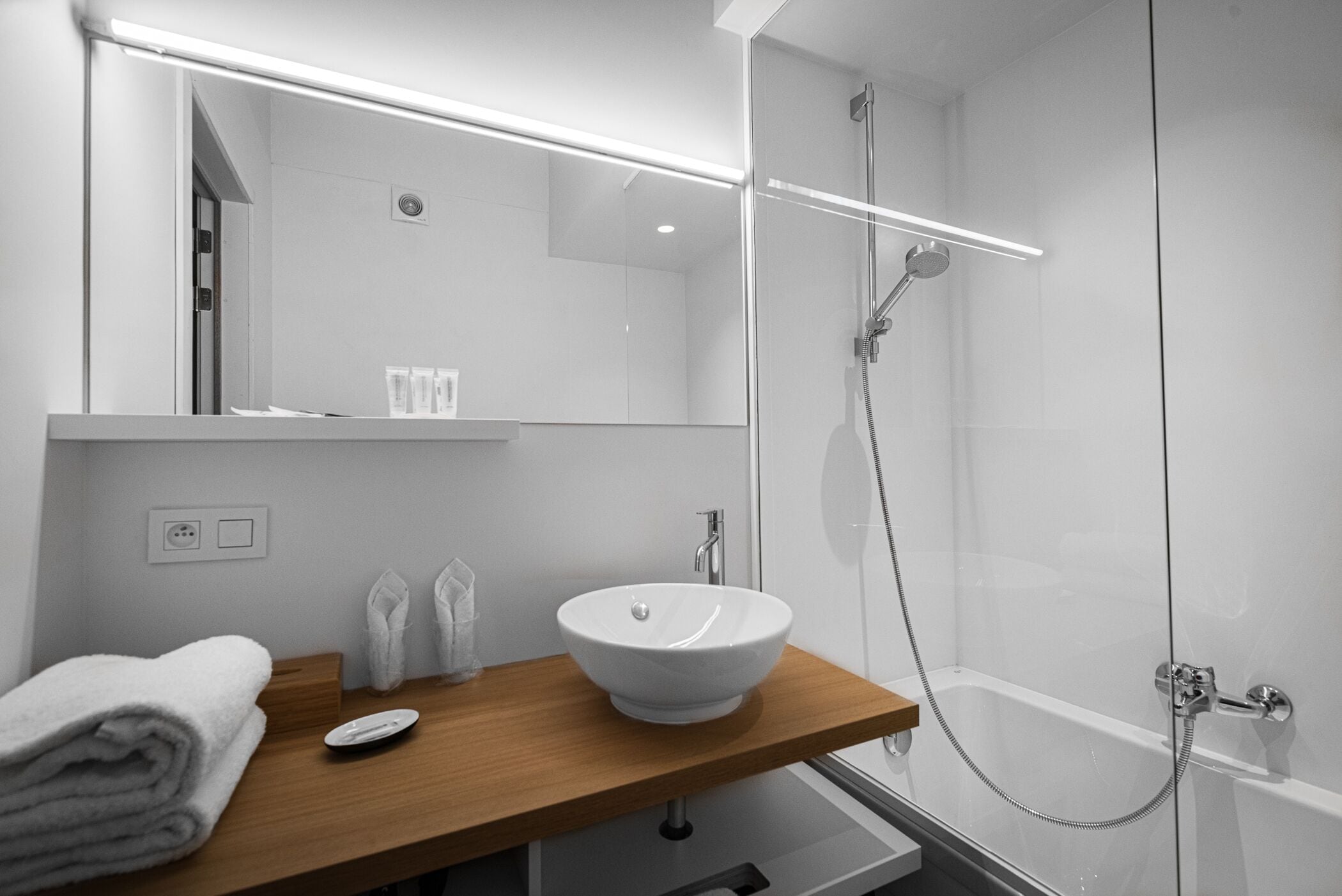 Un baño moderno con tocador de madera, un lavamanos blanco y ducha con cerramiento de vidrio.