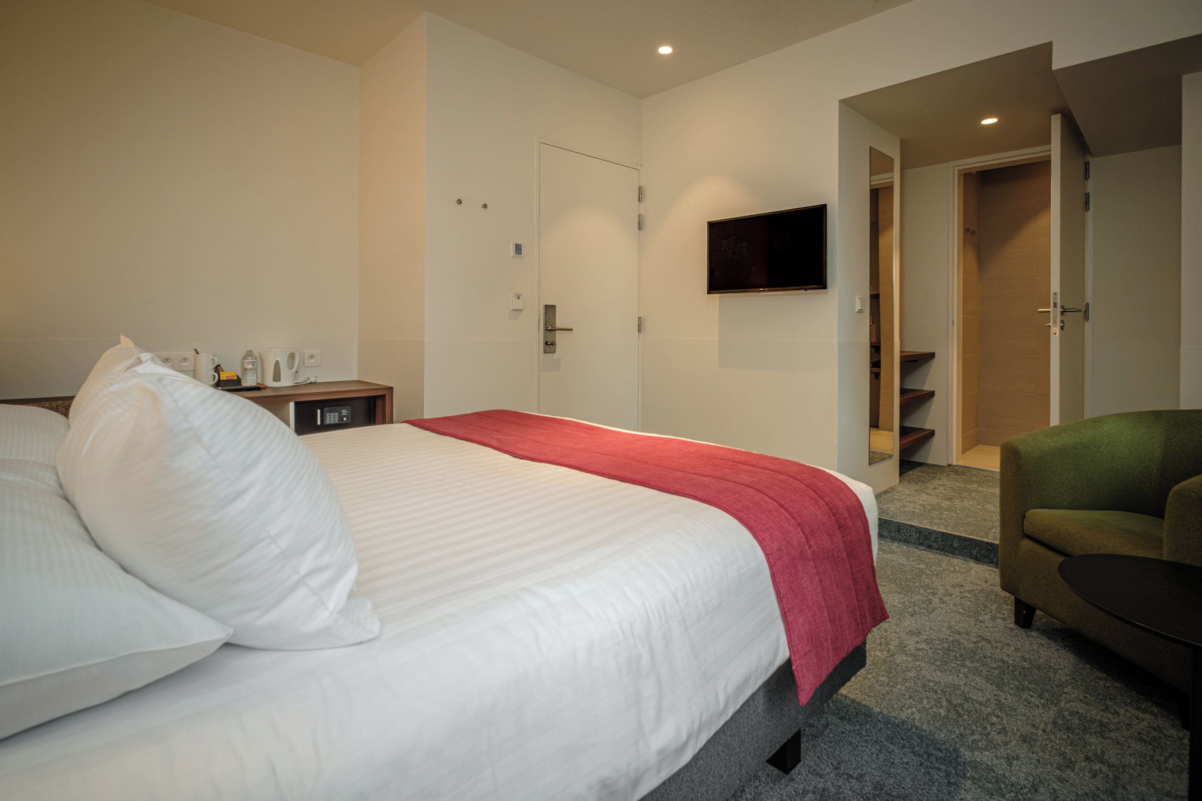 A hotel room with a bed, a TV mounted on the wall, a desk with a telephone, and a chair.