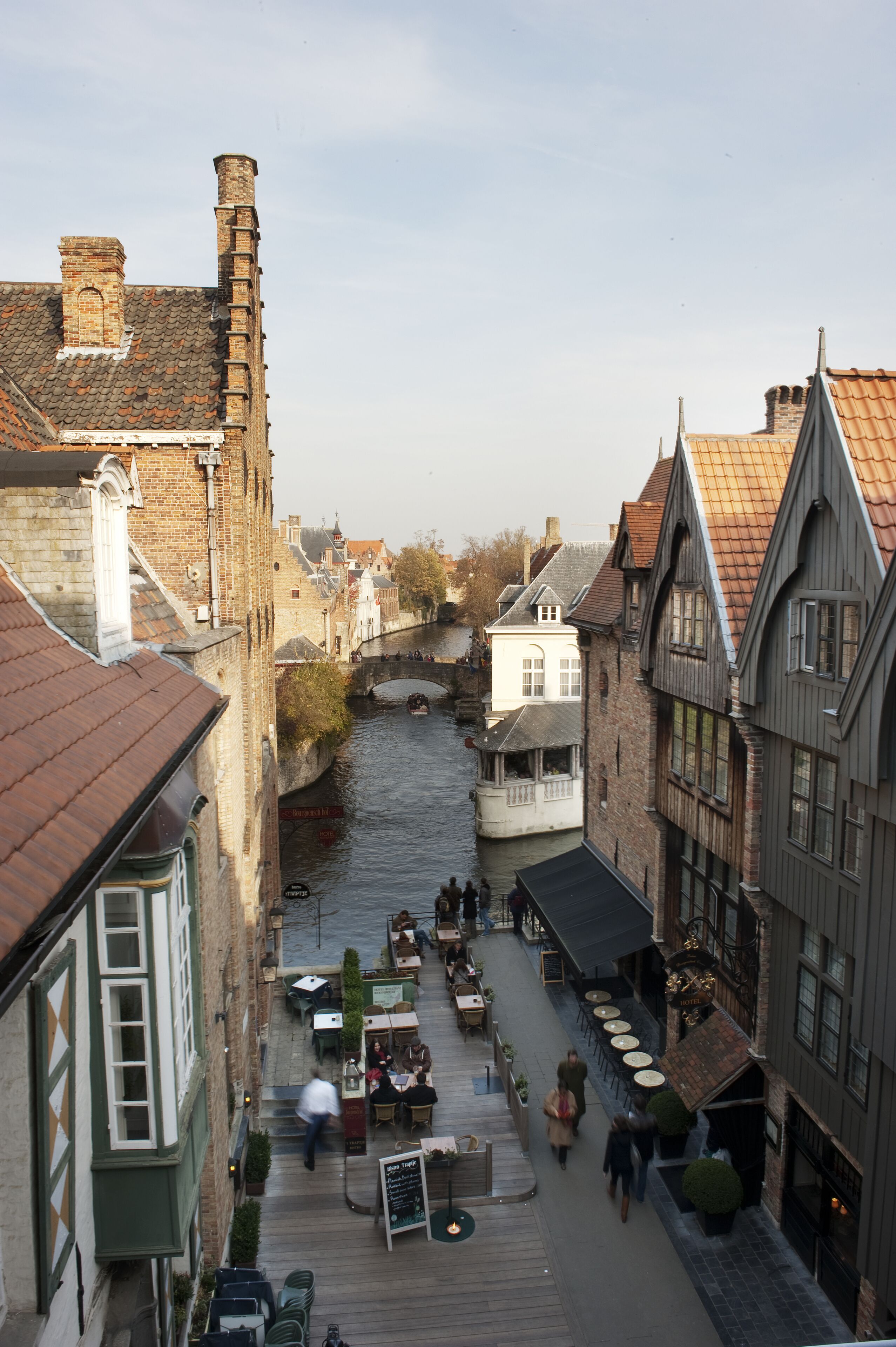 Una calle estrecha flanqueada por edificios, con un canal en el centro, zonas de estar al aire libre y algunas personas caminando.