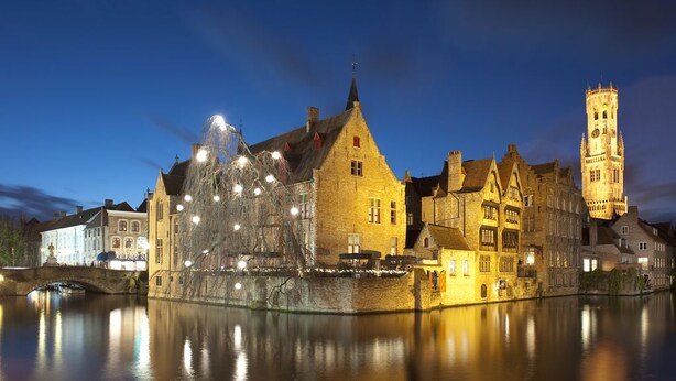 A historic town with a prominent tower and a bridge over a calm river.