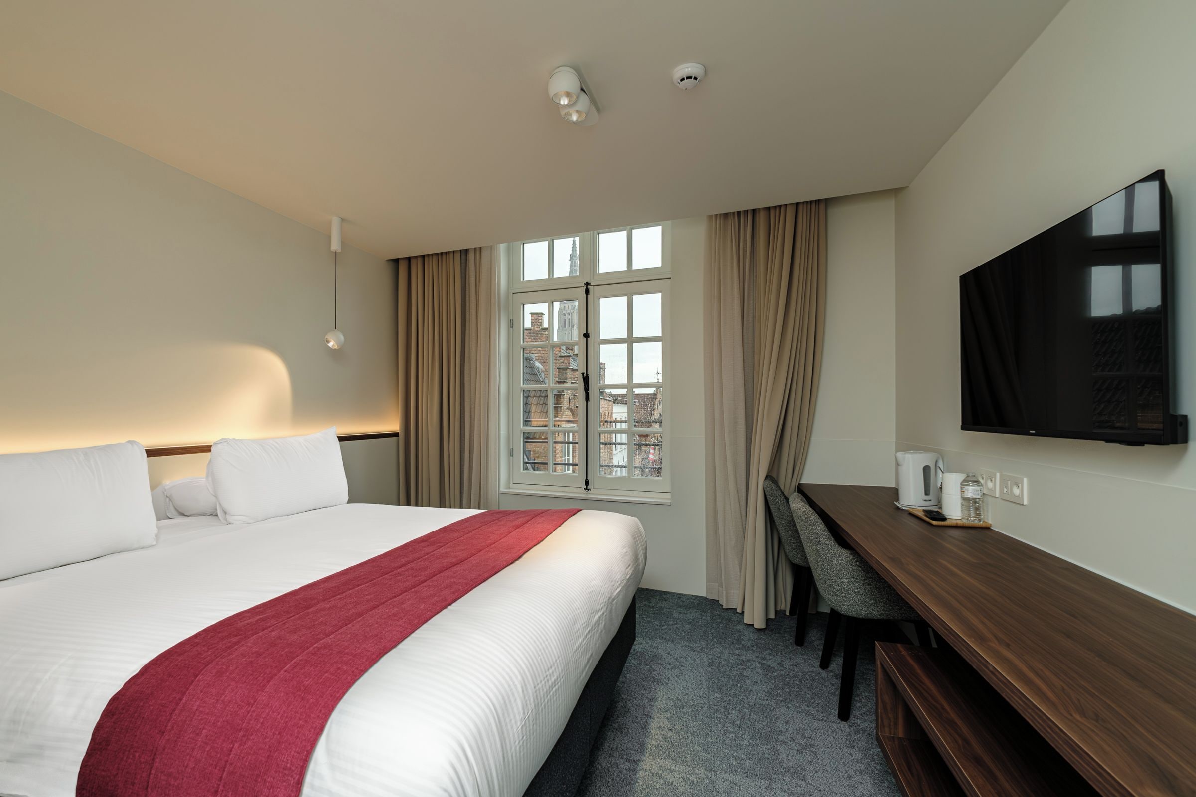 Une chambre d’hôtel avec un lit, un bureau, une télévision et une fenêtre avec des rideaux.