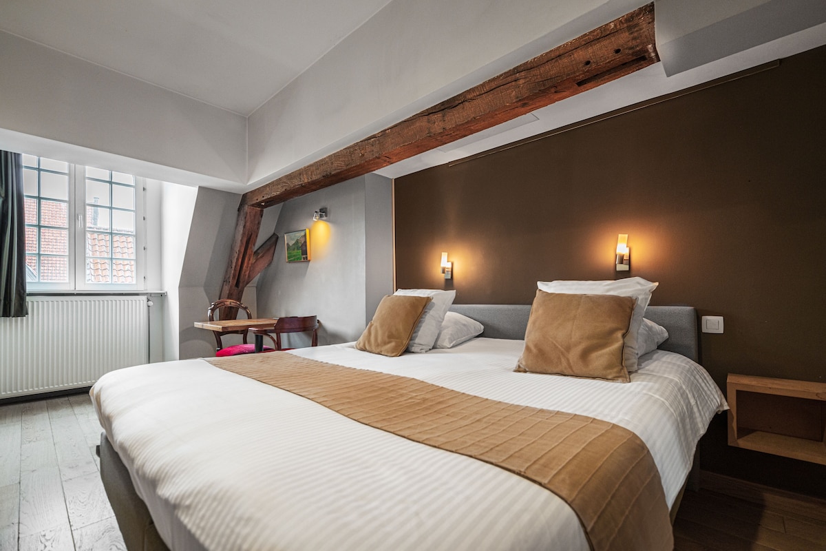 A bedroom with a large bed, two bedside tables, a wooden headboard, a desk, and a chair.
