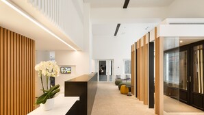 A modern reception area with a white reception desk, a potted orchid, and a wooden slatted wall.