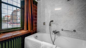 Une salle de bain moderne avec une baignoire, une fenêtre donnant sur des immeubles et un porte-serviettes.