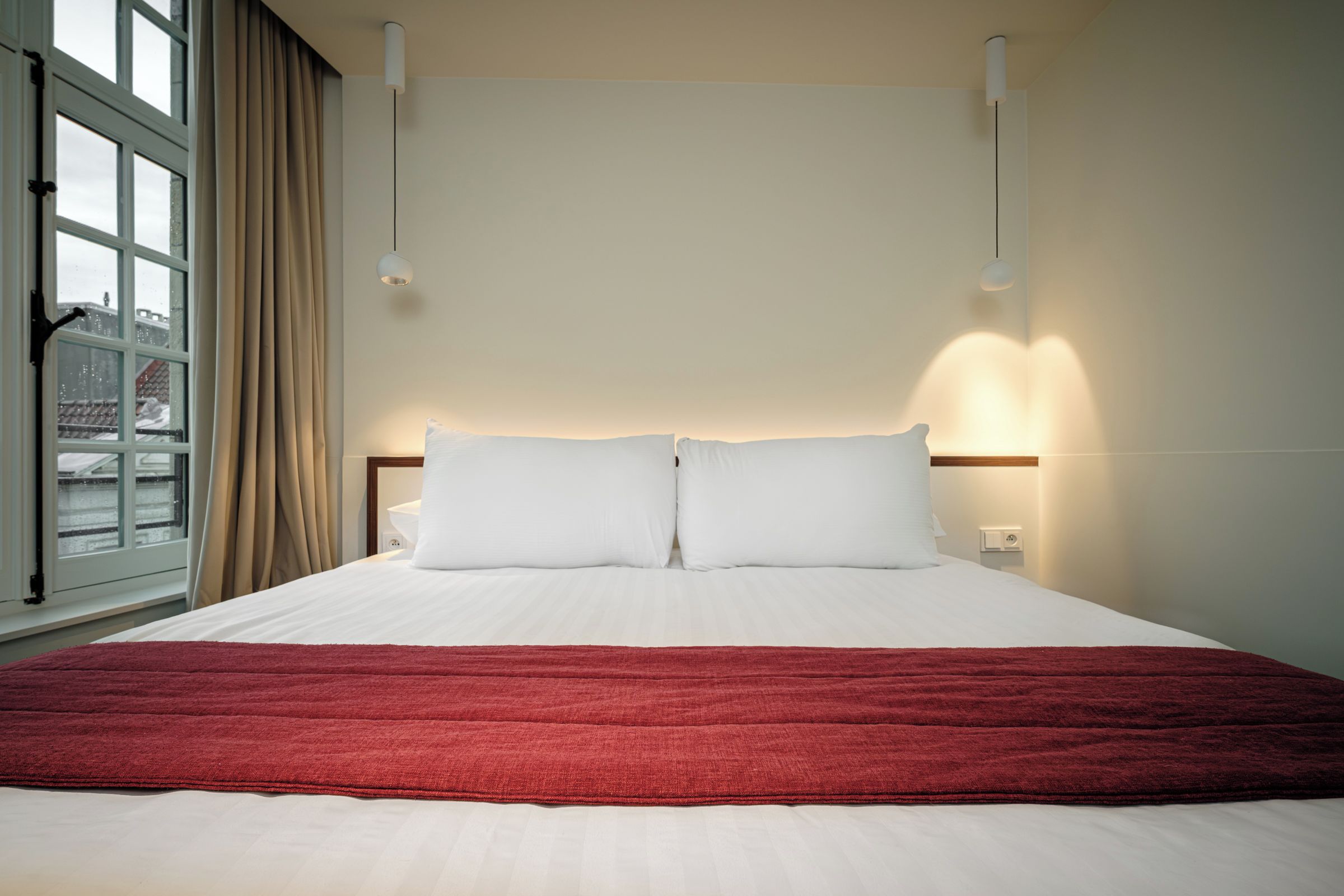 A hotel room with a large bed, a window with curtains, and a view of the city.